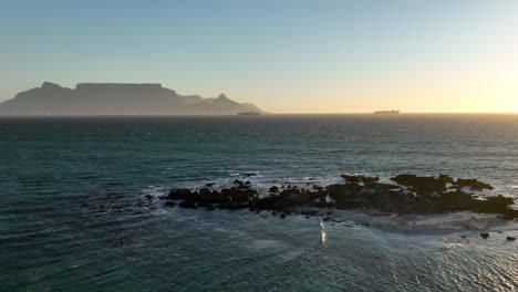 Drone-flight-above-rocky-rugged-reef-with-distant-sunset-view-of-Table-mountain
