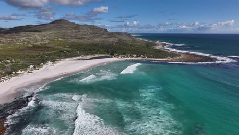 Schöne-Landschaftliche-Luftaufnahme-Eines-Strandes-Mit-Felsigen-Hügeln,-Meergrünem-Wasser,-Faulen-Wellen-Und-Teilweise-Bewölktem-Himmel-In-Der-Nähe-Von-Kapstadt-Südafrika