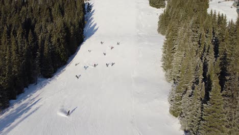 4k-Aerial-drone-of-group-of-people-skiing-down-a-snowy-mountain-piste-in-Norway-surrounded-by-trees-on-a-sunny-day
