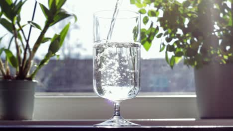 Die-Hand-Des-Mannes-Hält-Eine-Flasche,-Während-Er-Reines-Wasser-In-Transparentes-Glas-Gießt