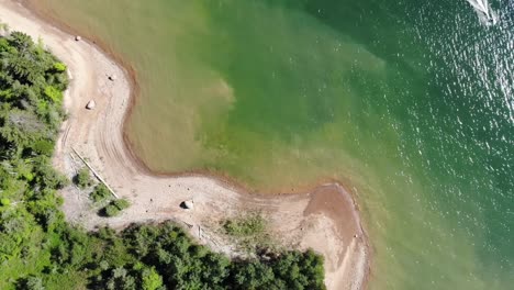 Aerial-footage-over-a-beach-on-a-green-lake,-looking-straight-down