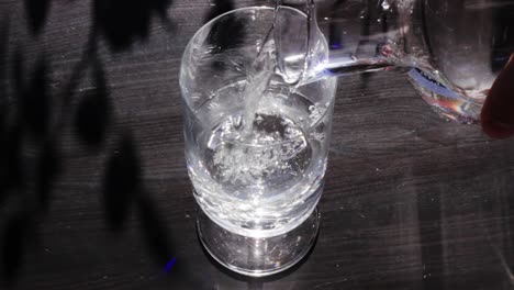 Drinking-glass-is-filled-with-fresh-water-from-decorative-glass-bottle