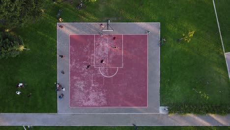 Aerial-top-down-circling-view-directly-above-pink-public-basketball-court-with-players-surrounded-by-green-area,-Buenos-Aires-in-Argentina