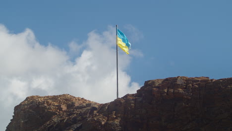Flag-of-Ukraine-Waving-in-Wind-on-Coastal-Rock-In-Cornwall,-England,-United-Kingdom--slow-motion