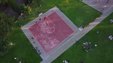 People-playing-on-pink-public-basketball-court-immersed-in-green-landscape,-Buenos-Aires-in-Argentina