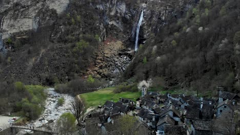 Aerial-flyover-over-Foroglio-in-Ticino,-Switzerland-with-a-view-of-the-village-with-old-stone-houses-and-waterfall-in-the-background-at-dusk