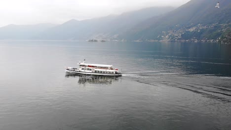 Aerial-view-alongside-a-boat-cruising-on-Lago-Maggiore-near-Ascona-in-Ticino,-Switzerland-with-seagulls-flying-alongside-and-a-view-of-the-Swiss-Alps-on-a-cloudy-day
