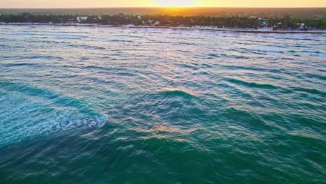 Drone-Flying-Over-Vibrant-Turquoise-Blue-Ocean-Water-Waves-Near-Carribean-Beach-In-Mexico-During-Sunset