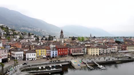 Aerial-view-of-Ascona-in-Ticino,-Switzerland-at-the-shore-of-Lago-Maggiore-with-a-pull-away-movement-revealing-the-rooftops,-lake-and-mountains-in-the-background-from-a-higher-elevation
