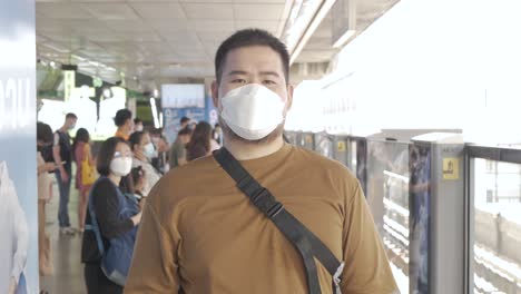 Ein-Mann-Mit-Maske,-Der-Handy-Spielt,-Während-Er-Auf-Den-Zug-Der-öffentlichen-Verkehrsmittel-Der-U-bahn-In-Bangkok-Wartet