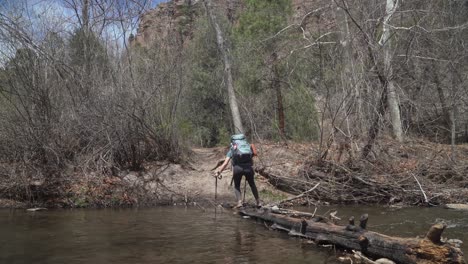 Female-backpacker-carefully-crosses-stream-on-log-while-hiking-in-New-Mexico