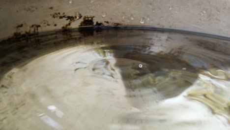 Macro-closeup-of-drop-of-water-leaking-from-pipe-inside-bucket,-costant-ripples