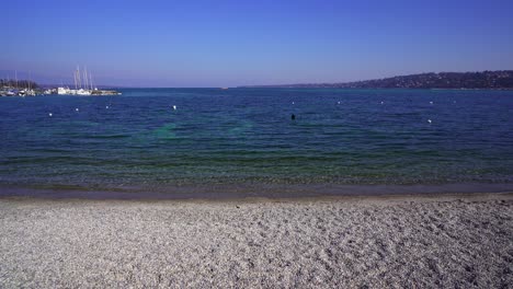 Geneva,-the-small-pebble-beach-on-Bains-des-Pâquis-looking-out-toward-Lake-Geneva