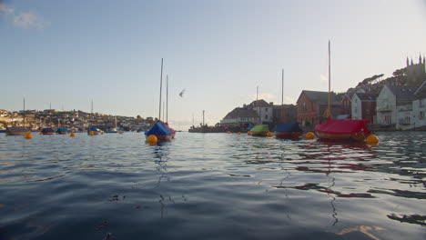 Seagull-Flying-Over-Moored-Sail-Boats-Floating-in-River-Fowey,-Cornwall,-low-angle-wide