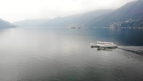 Luftaufnahme-Eines-Bootes,-Das-Auf-Dem-Lago-Maggiore-In-Der-Nähe-Von-Ascona-Im-Tessin,-Schweiz,-Mit-Blick-Auf-Die-Schweizer-Alpen-Und-Das-Stadtufer-Im-Hintergrund-Fährt