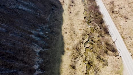 Drone-footage-of-the-mountain-shade,-small-river-and-a-car-passing-by-on-the-road