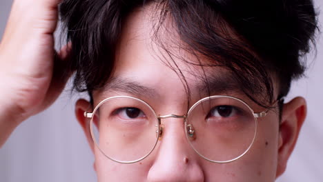 Nahaufnahme-Asiatischer-Mann-Mit-Brille-Und-Gesundem-Gutem-Haar,-Der-In-Die-Kamera-Schaut-Und-Sich-Selbst-Verwöhnt,-Indem-Er-Seine-Haare-Aufräumt