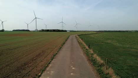 Niedrige-Drohnenantenne-über-Einem-Feldweg-In-Yorkshire-In-Richtung-Windkraftanlagen,-Die-Grüne-Energie-Produzieren