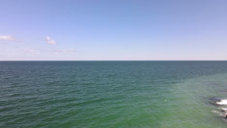 Greenish-ocean-water-around-submerged-ledge,-aerial-push-forward,-horizon-in-middle-of-the-frame