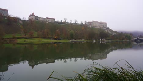 Castillo-De-Burghausen-En-La-Niebla,-Toma-Panorámica-Lenta-Que-Revela-El-Castillo-Más-Largo-Del-Mundo-Reflejado-En-Un-Lago