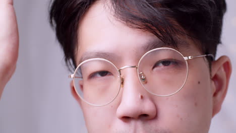 Nahaufnahme-Asiatischer-Mann-Mit-Brille-Und-Gesundem-Gutem-Haar,-Der-In-Die-Kamera-Schaut-Und-Sich-Selbst-Verwöhnt,-Indem-Er-Seine-Haare-Aufräumt
