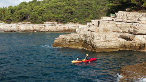 View-Of-Travelers-Kayaking-Near-Cliffs-And-Caves-Of-Pula,-Istria,-Croatia---drone-shot