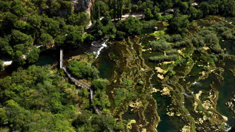 Roski-wasserfall---Brücke-Bei-Roski-Slap-Mit-üppigen-Grünen-Pflanzen-Und-Algen-An-Einem-Sonnigen-Tag-In-Kroatien