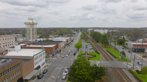 Aerial-boom-down-over-downtown-Thomasville,-North-Carolina-over-main-street-with-store-fronts-and-train-tracks-and-a-water-tower