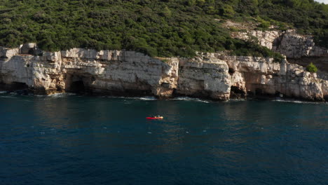 Kayak-Riding-Near-Cliffs-And-Caves-In-Pula,-Istria,-Croatia---aerial-drone-shot
