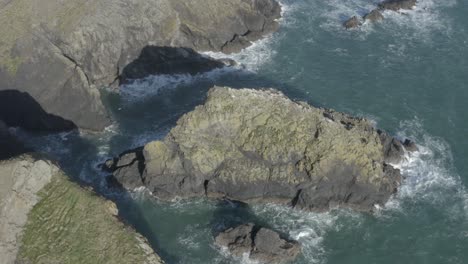 Ocean-waves-crash-against-and-birds-land-on-rugged-rocky-coast-islet