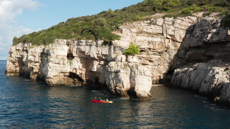 Gente-Haciendo-Kayak-En-Aguas-Azules-Cerca-De-Acantilados-En-Pula,-Istria,-Croacia---Toma-Aérea-De-Drones