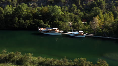Two-Boats-Carrying-Tourists-Dock-At-Terminal-With-Green-Forest-At-Krka-National-Park-In-Croatia