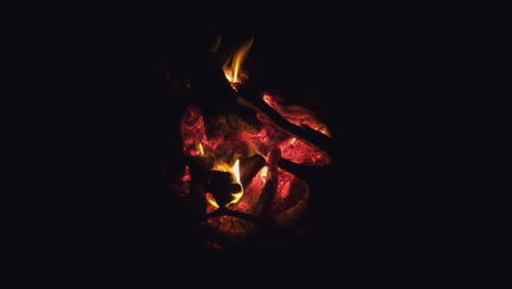 Glowing-orange-campfire-embers-and-flames-burning-in-black-of-night