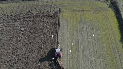 Aerial-view:-Tractor-with-disc-harrow-turns-packed-soil-in-green-field