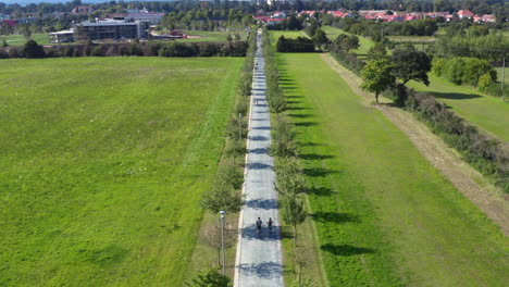 Couple-cycling-side-by-side-on-countryside-village-road,-drone-shot