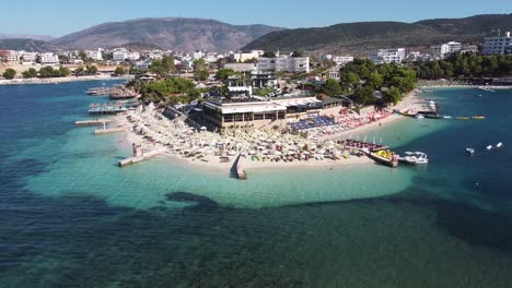 Ksamil,-Albania---Reversing-Aerial-of-Popular-Holiday-Destination-with-Beach,-Sea,-Hotels-and-Sunbeds