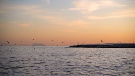 View-out-towards-silhouetted-lighthouse-with-birds-flying-at-sunset
