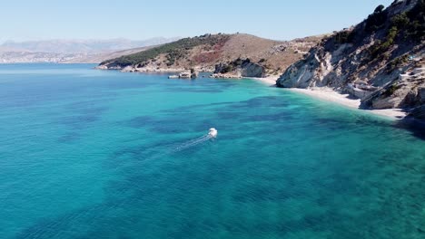 Barco-Navega-En-Un-Mar-Azul-Claro-A-Lo-Largo-De-La-Costa-De-Ksamil,-Albania---Antena