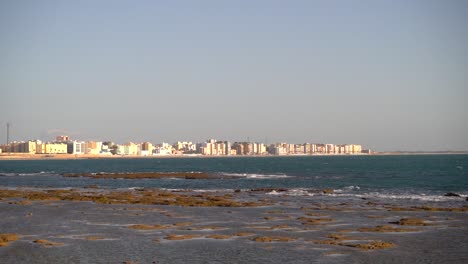Low-tide-ocean-with-waves-breaking-and-white-city-in-distance