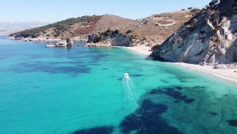 El-Barco-Navega-Sobre-El-Azul-Claro-Del-Mar-Jónico-Para-Reflejar-La-Playa-En-Ksamil,-Albania---Seguimiento-De-Dolly-Aéreo