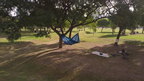Zoom-out-shot-of-brunette-woman-lying-in-hammock-in-park-during-sunny-day