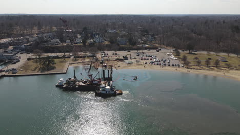 Aerial-pullback-from-boat-launch-where-a-tug-boat-and-barge-move-in-harbor