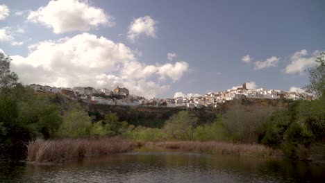 Pan-across-small-pond-looking-out-towards-white-washed-Spanish-village-on-hill