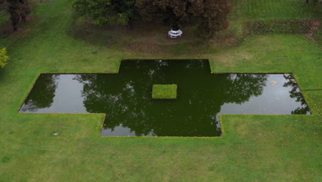 Dark-reflection-on-a-cross-shaped-pond-near-Castle-Bon-Repos,-wedding-destination,-aerial-down-tilt-up