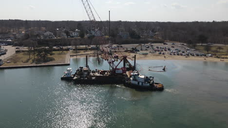 Aerial-circle-panning-shot-of-harbor-setting-with-tugboat-and-barge-with-crane-attached