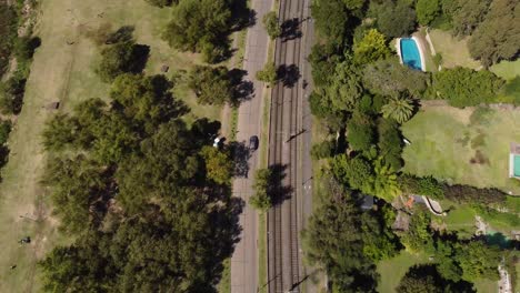 Aerial-top-down-shot-of-car-driving-on-street-beside-railroad-during-sunlight-in-Buenos-Aires-City