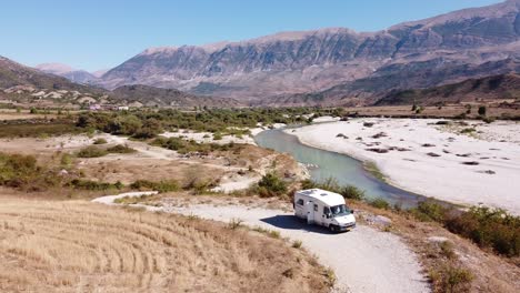 Vanlife-in-Gjirokaster,-Albania---Motorhome-stays-along-Dron-River-and-Mountains---Aerial-Circle-Shot
