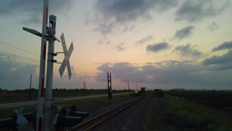 Luftaufnahme,-Vorbei-An-Einem-Bahnübergangsschild-Und-Folgenden-Spuren-Bei-Sonnenuntergang-In-Texas,-U
