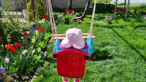 Back-view-of-a-cute-little-girl-with-a-pink-hat-on-a-swing-in-the-backyard
