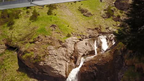 View-of-a-waterfall-followed-by-a-view-of-a-bridge-that-crosses-the-river-in-the-Swiss-alps